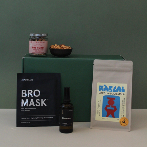 Collection of skincare product, coffee, and snacks on a green box against a green background