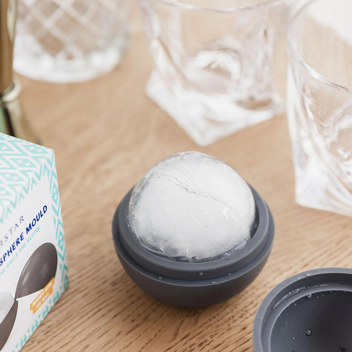 Ice cube tray with a frozen ice ball on a wooden surface