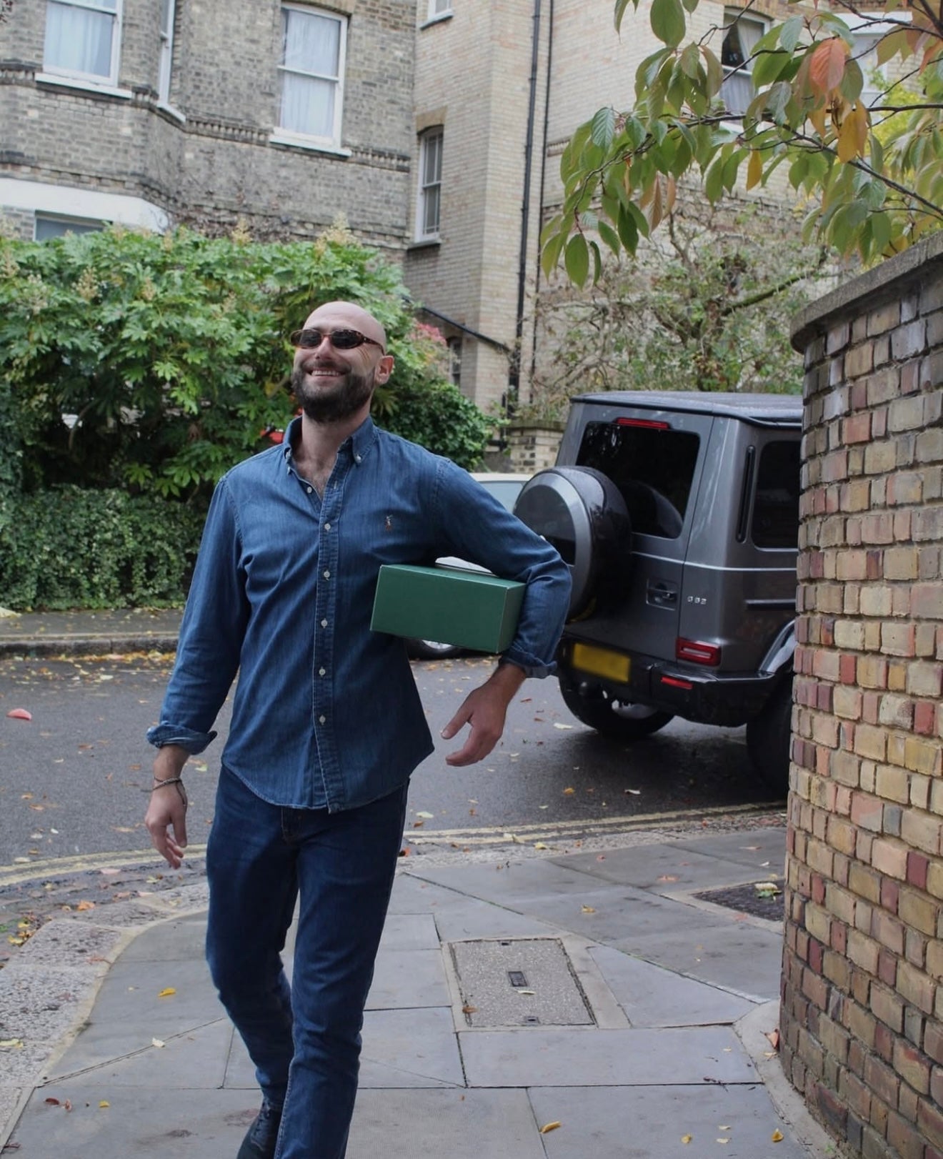 Man walking with a green box on a street, with a van in the background.