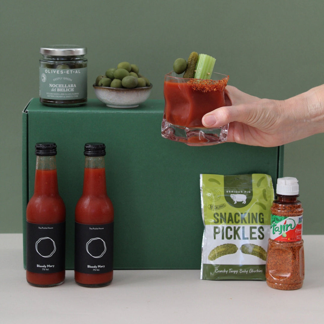 Hand holding a Bloody Mary with olives, pickles and spice